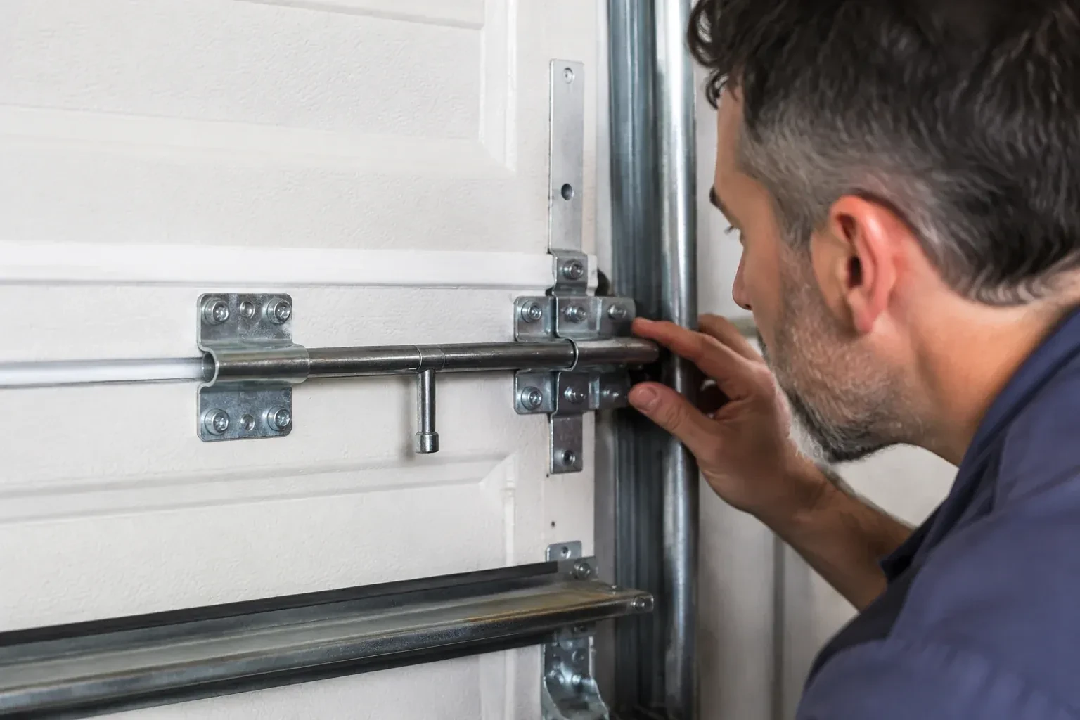 Person leaning close to a white paneled door, one hand on a metal slide-bolt bar mounted across the panel. — Garage Door Manual Lock Repair, Hamilton