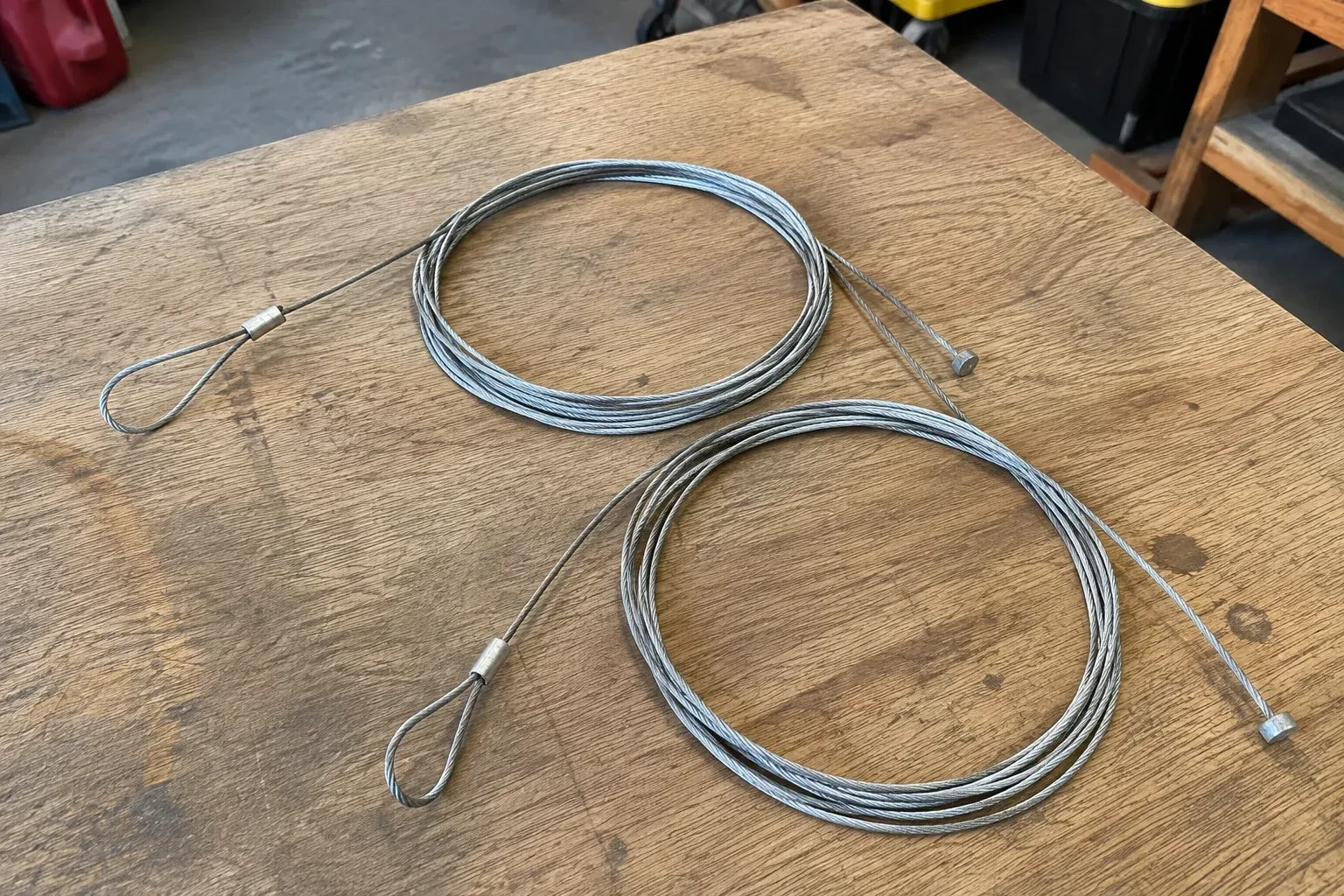 Two coiled steel cables with loop and stop ends on a workbench. — Garage Door Cable Replacement, Hamilton