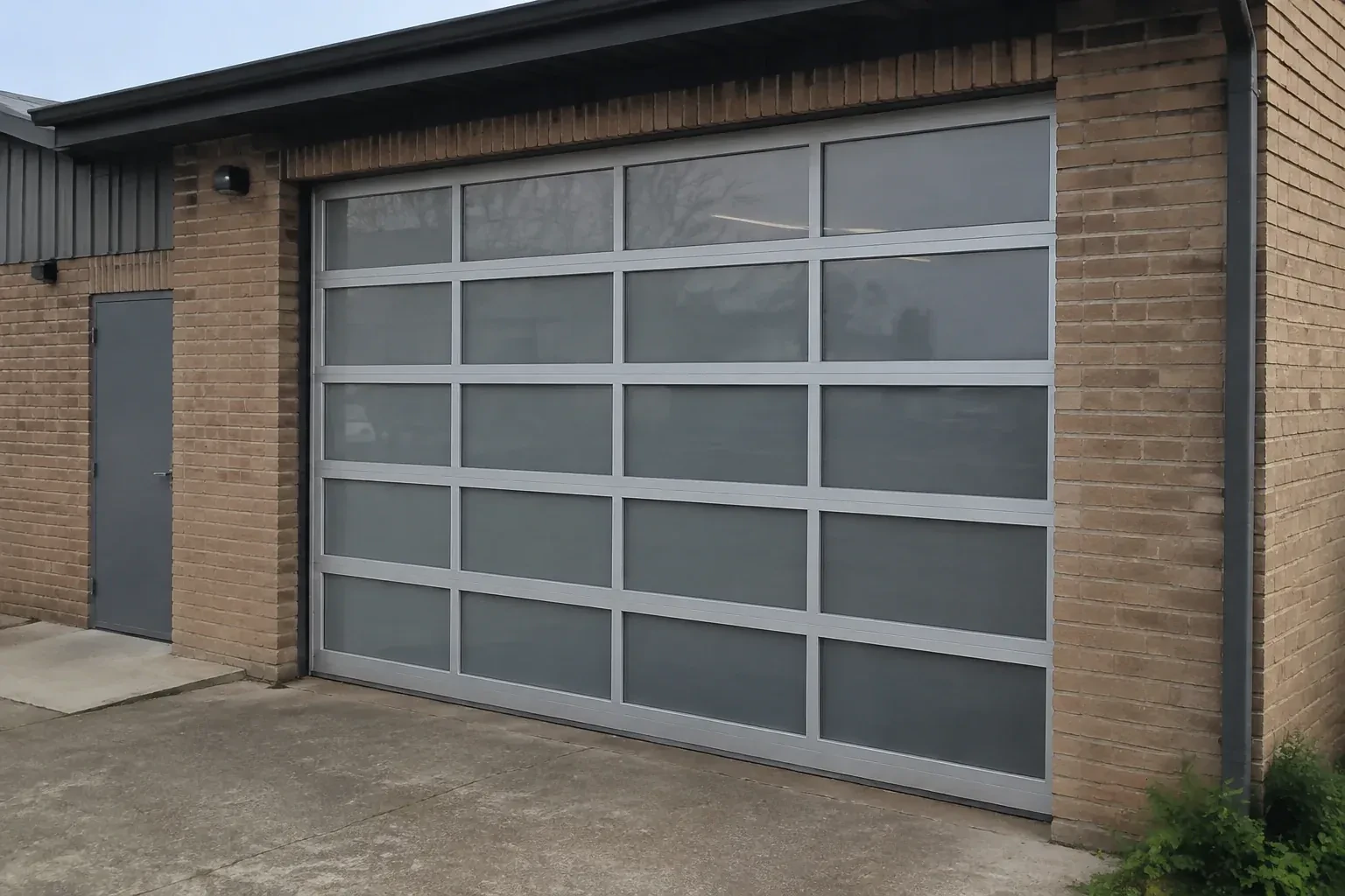 Closed glazed sectional door in a grey metal frame at a brick workshop. — Full-View Glass Garage Door Installation, Hamilton